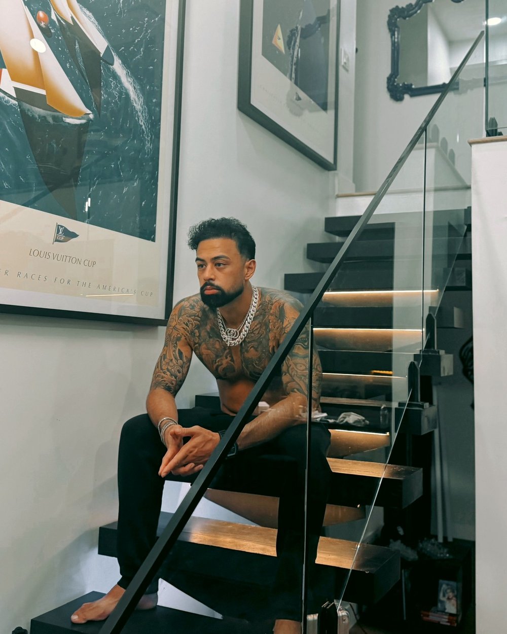 Evan Valdes sitting barefoot on a black staircase, tattooed and wearing silver chains